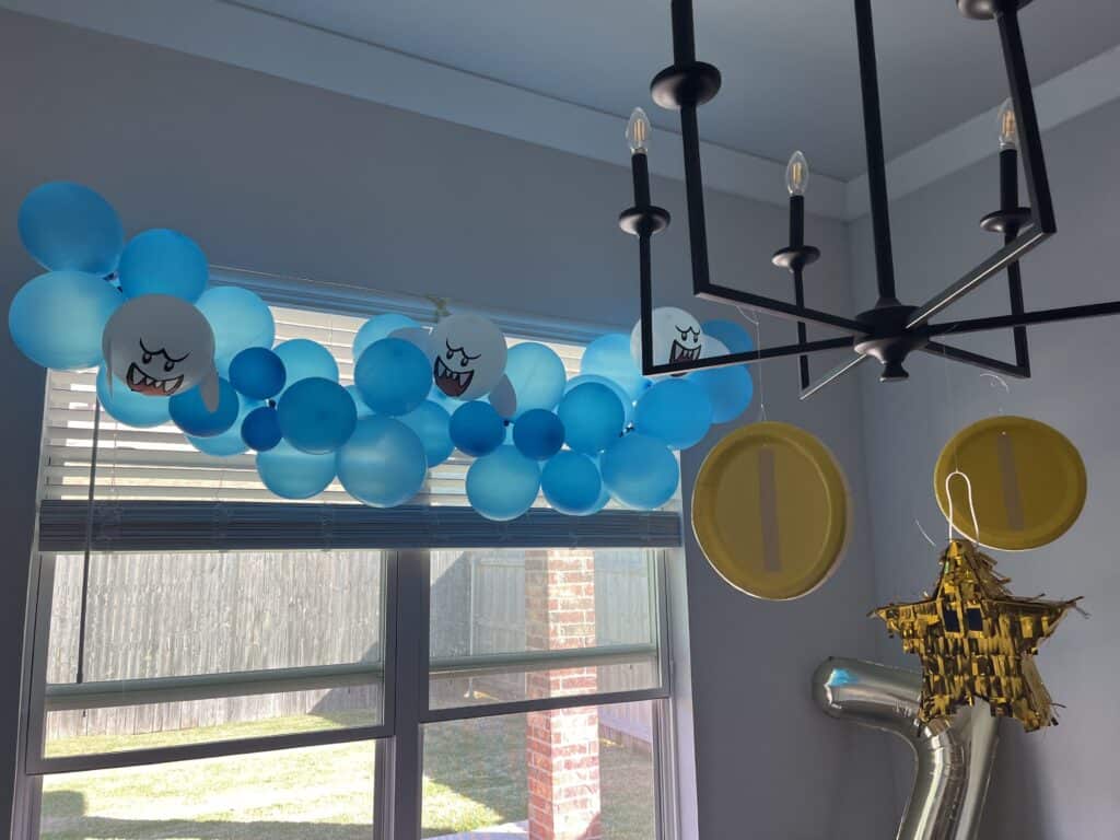 diy mario birthday party decorations that include boo ghosts, mario coins, star, and number 7 balloon