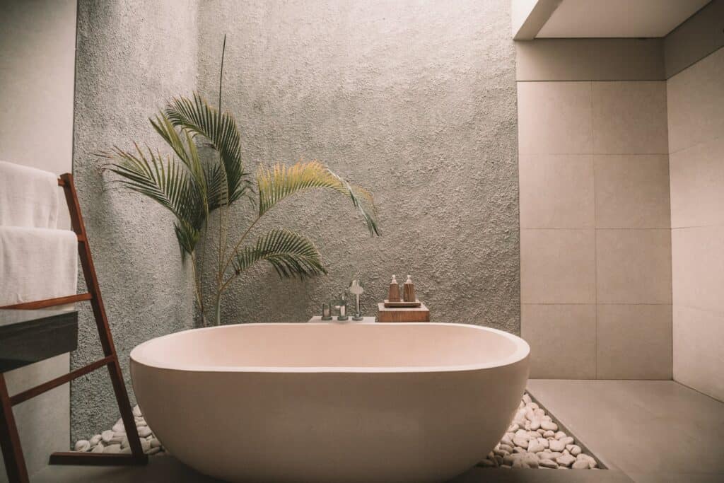 luxury bath rug featured image of high-end stand along bathtub with cement walls and tropical plant on left corner